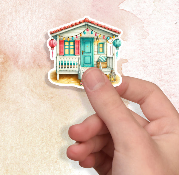 Hand holding a small house-shaped sticker with colorful decorations on a textured beige background