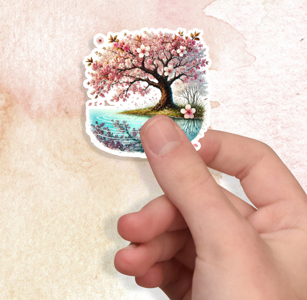 Hand holding a sticker of a cherry blossom tree by a lake on a textured beige background