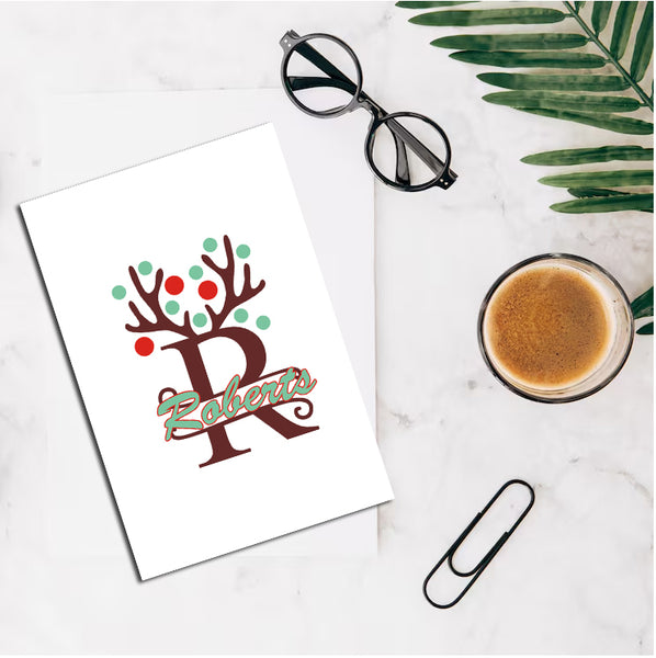 Letter 'R' with decorative elements on a card, next to a cup of coffee and glasses on a marble surface.