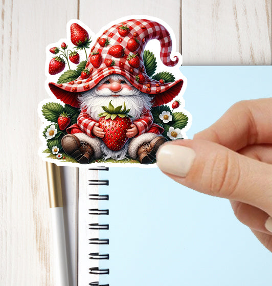 Sticker of a gnome with a red checkered hat holding strawberries, held over a notebook.