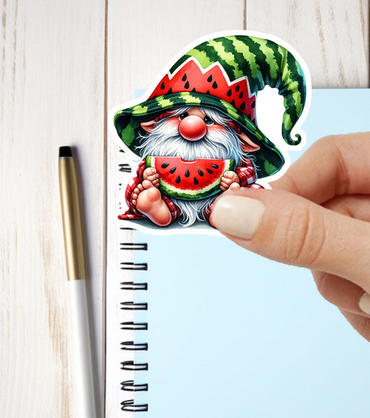 Sticker of a gnome with watermelon hat and watermelon slice held by a hand, on a notebook.