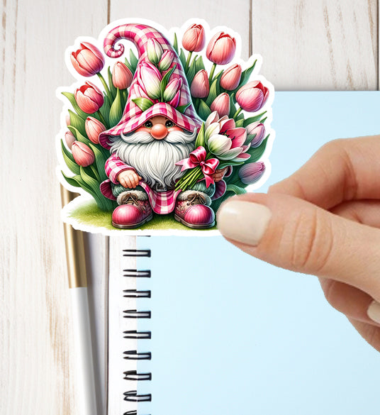 Sticker of a gnome with pink hat and flowers held over a notebook