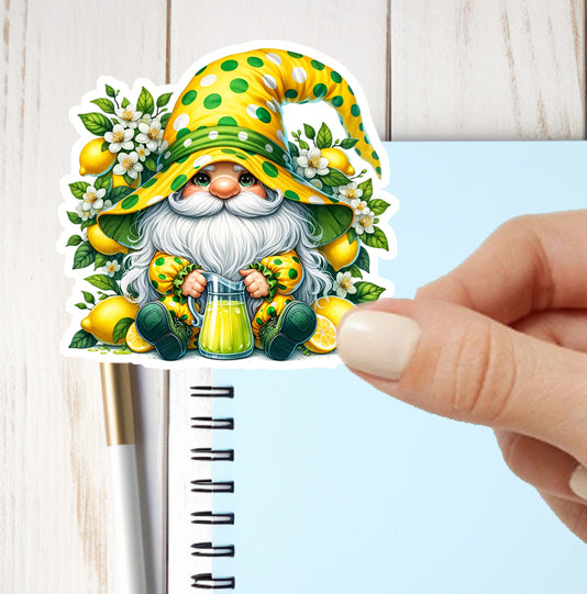 Sticker of a gnome holding lemons and flowers, held by a hand over a notebook.