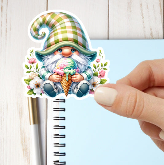 Hand holding a decorative sticker of a gnome with a ice cream cone on a notebook.