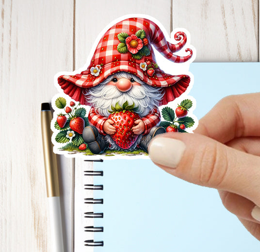 Sticker of a gnome holding strawberries on a notebook with a hand holding it.