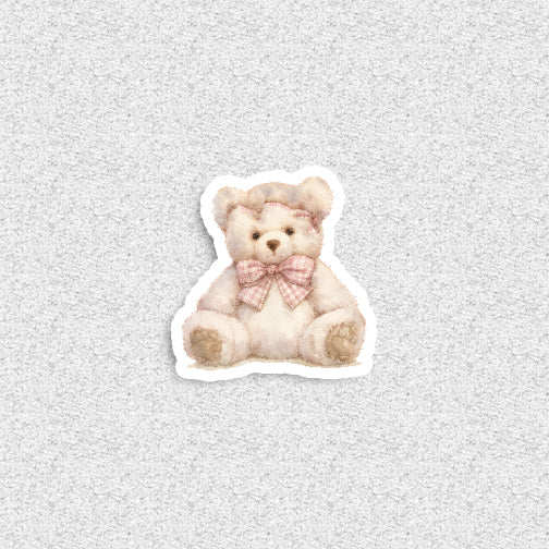 Sticker of a teddy bear with a pink bow on a textured gray background