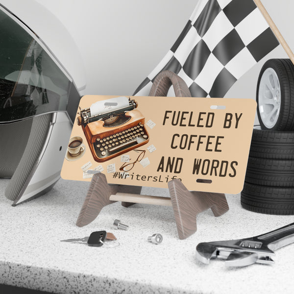 License plate with typewriter design and text 'Fueled by Coffee and Words' on a desk with tools and a helmet.