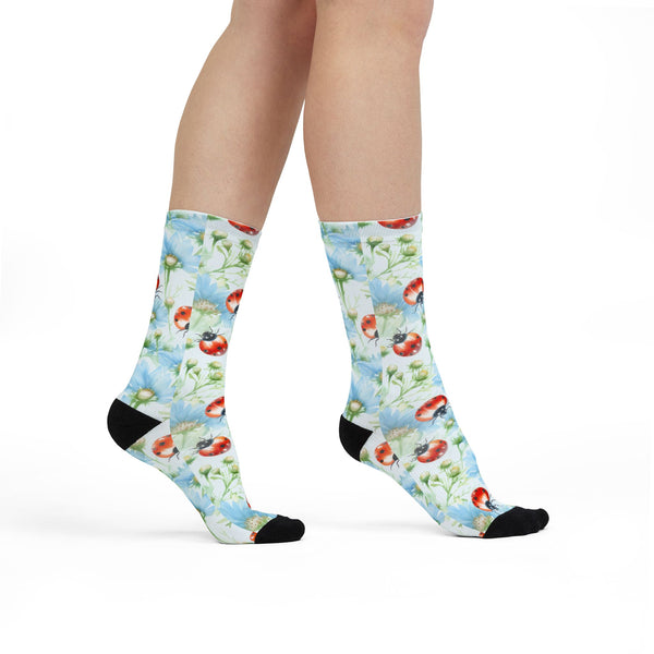Colorful socks with floral and ladybug pattern worn by a person on a white background