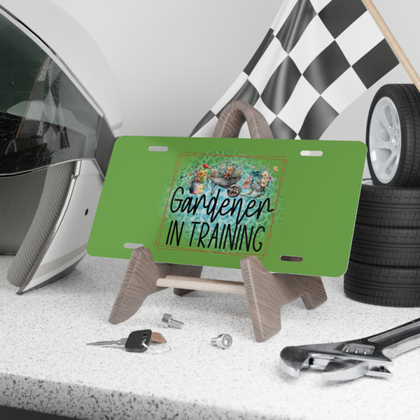 Green license plate with 'Gardener in Training' text on a stand, surrounded by tools and a helmet.