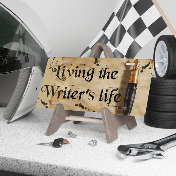 License plate with 'Living the Writer's Life' text in a garage setting with tools and a helmet.