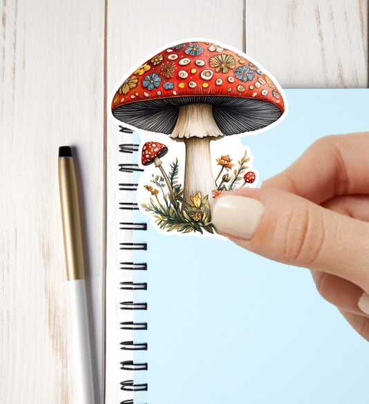 Colorful mushroom sticker being placed on a notebook with a pen next to it.