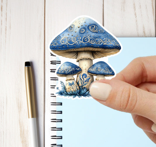 Decorative sticker of blue mushrooms with a hand holding it over a notebook.