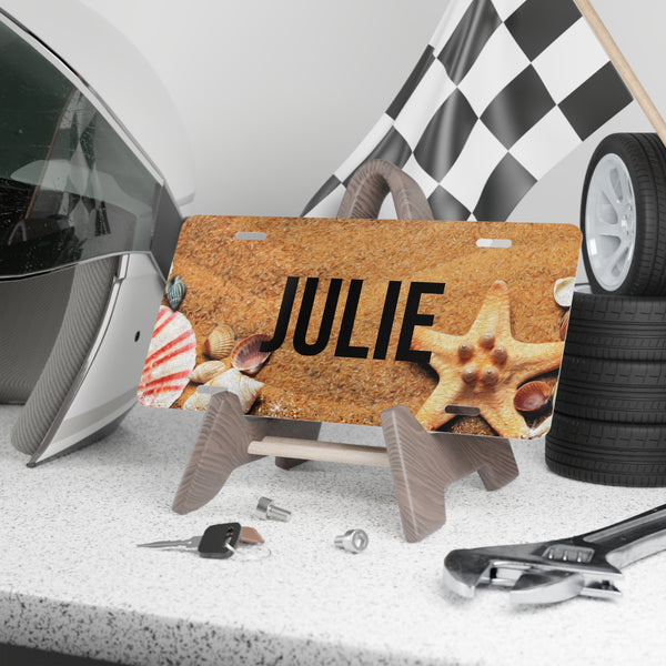 Personalized license plate with 'JULIE' on a cork background, surrounded by car parts and tools.