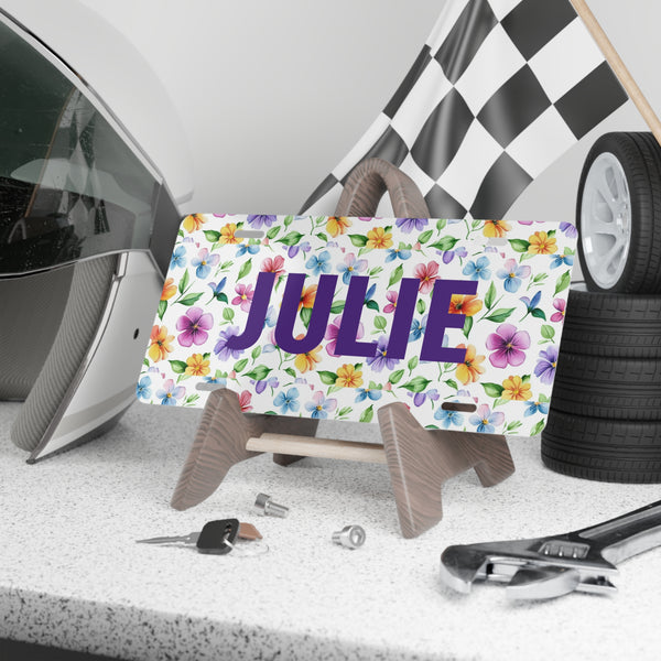 Decorative license plate with 'JULIE' and floral design on a stand, with car parts in the background.