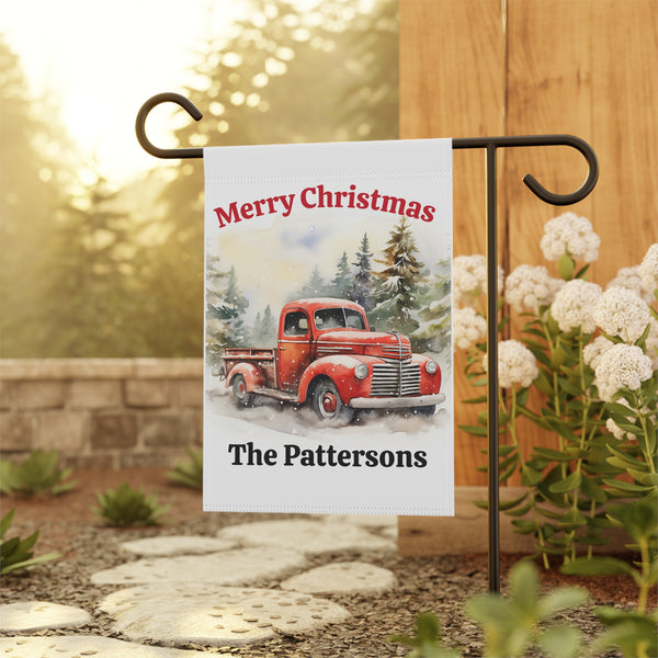 Christmas garden flag with a red truck and personalized text, displayed outdoors.
