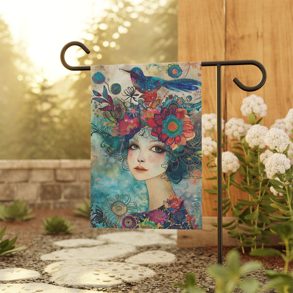 Decorative garden flag with a colorful design of a woman's face and flowers, displayed outdoors.