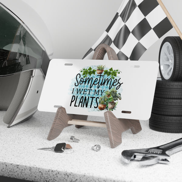 License plate with 'Sometimes I Wet My Plants' text and plant graphics on a stand, with car parts in the background.