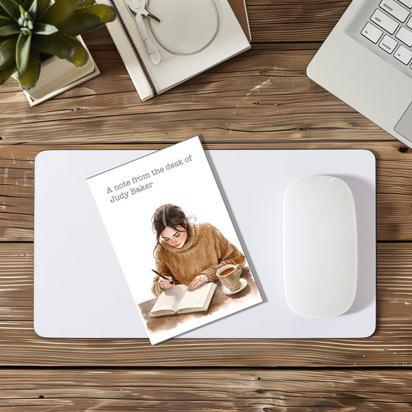 Personalized mouse pad with a photo of a woman reading a book and a cup of coffee, placed on a wooden desk.